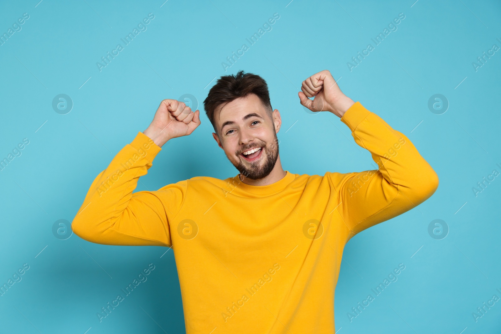 Photo of Excited man in yellow sweatshirt celebrating victory on light blue background
