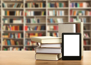 Hardcover books and modern e-book on wooden table in library. Space for text