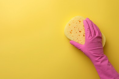 Cleaner in rubber glove holding new sponge on yellow background, top view. Space for text