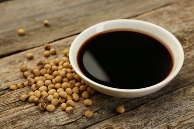 Photo of Soy sauce in bowl and beans on wooden table, closeup