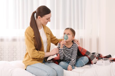 Mother helping her sick daughter with nebulizer inhalation in bedroom