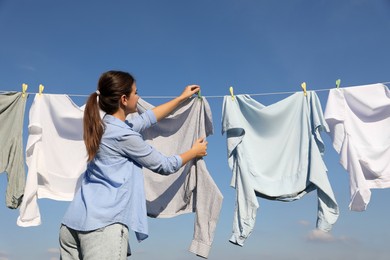 Photo of Woman hanging clothes with clothespins on washing line for drying against blue sky