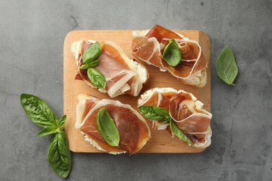Photo of Tasty sandwiches with cured ham and basil on grey table, flat lay