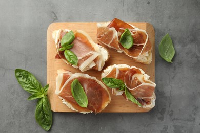 Tasty sandwiches with cured ham and basil on grey table, flat lay