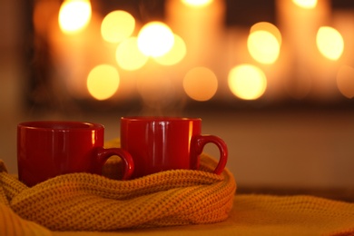 Cups of hot drink on knitted scarf against blurred background. Winter atmosphere