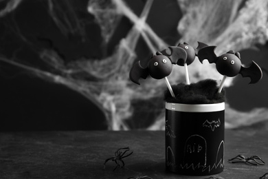 Bat shaped cake pops on black table, space for text. Halloween treat