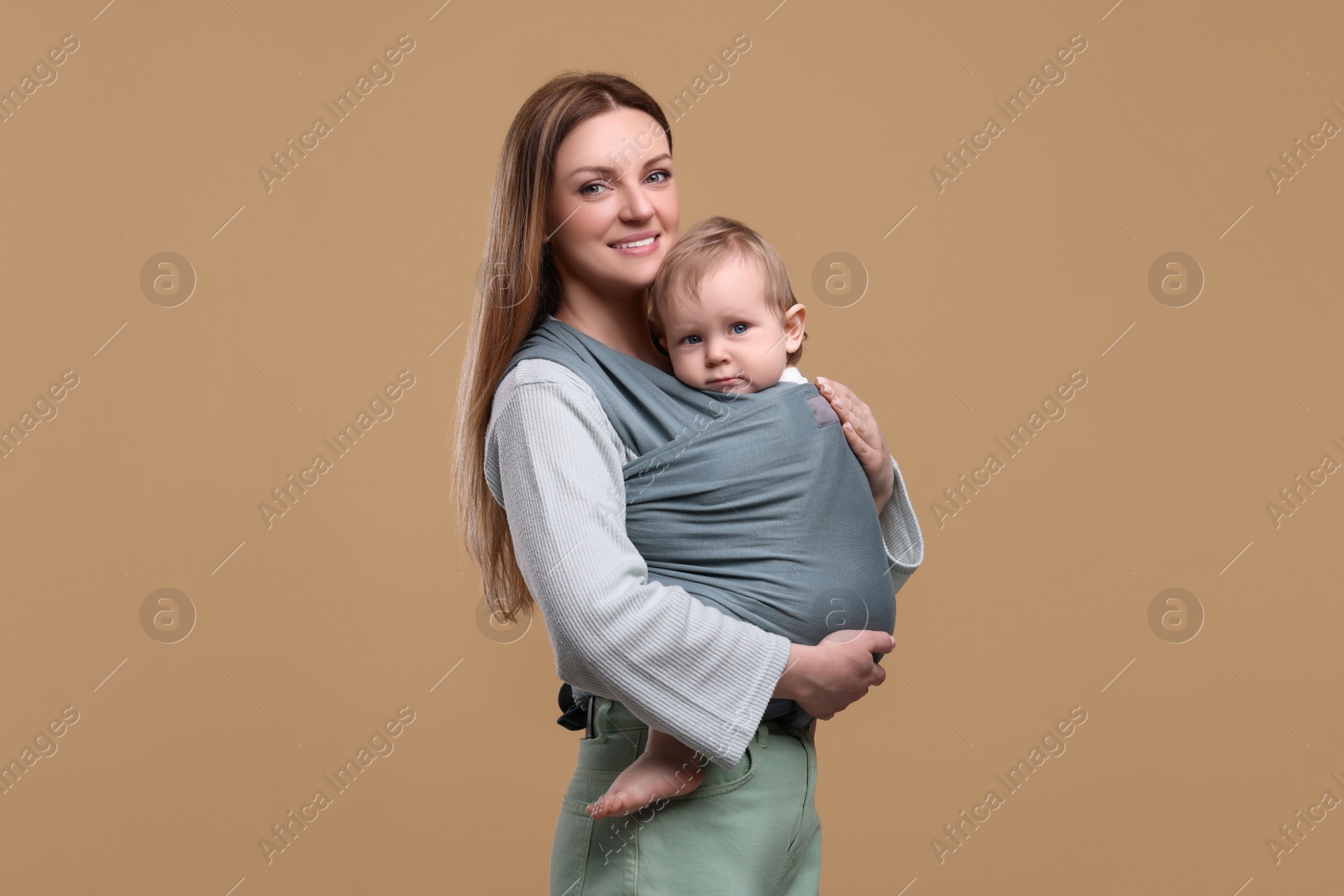 Photo of Mother holding her child in baby wrap on light brown background