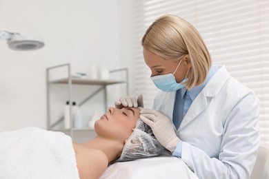 Photo of Dermatologist in medical mask examining patient`s face in clinic
