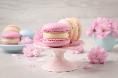 Delicious colorful macarons and pink flowers on light grey table