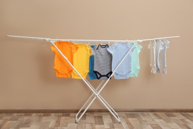 Photo of Different cute baby onesies hanging on clothes line near beige wall. Laundry day
