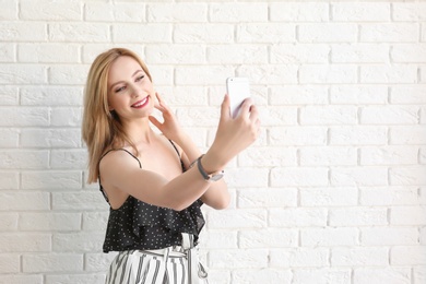 Attractive young woman taking selfie near brick wall