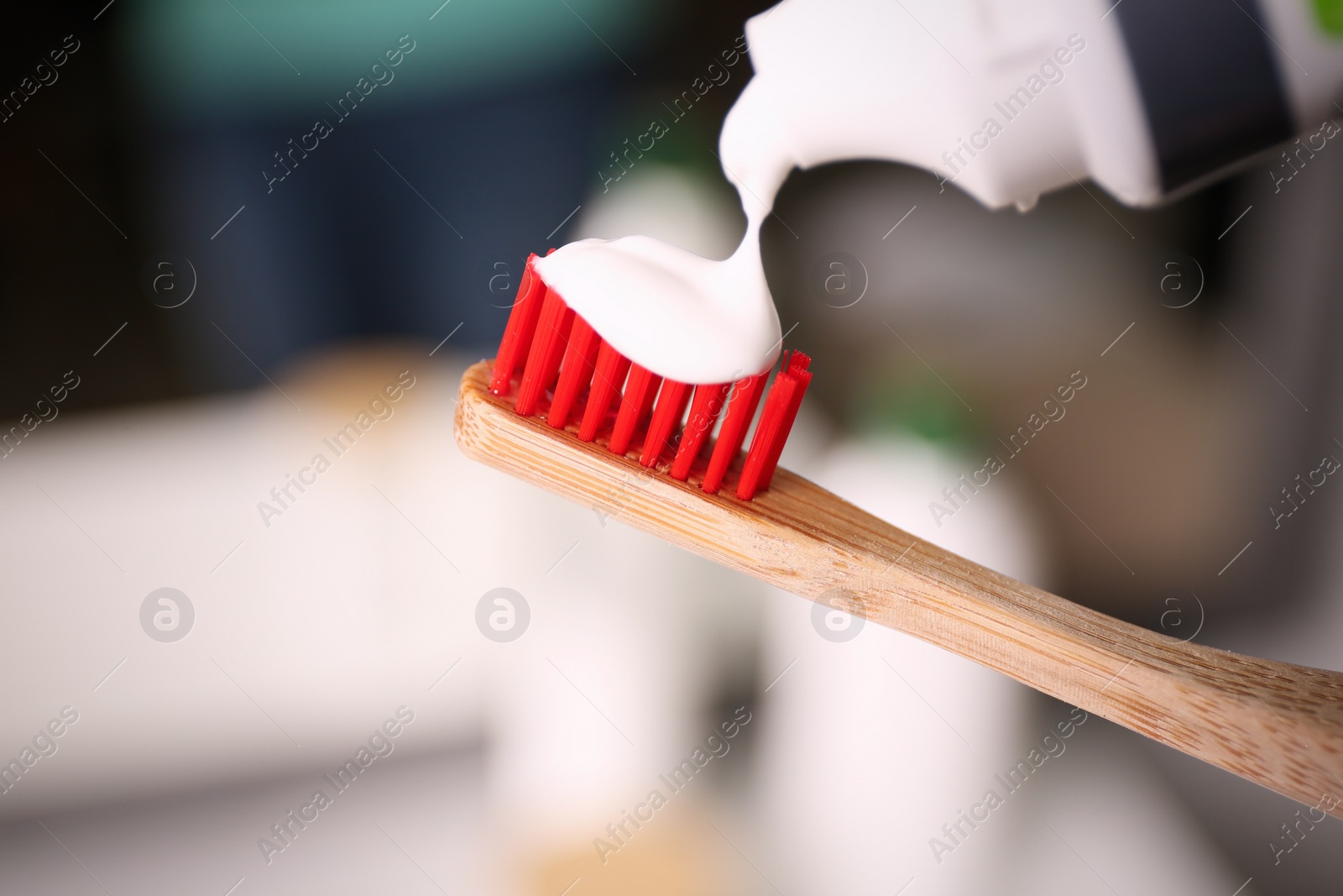 Photo of Applying toothpaste on brush against blurred background, closeup