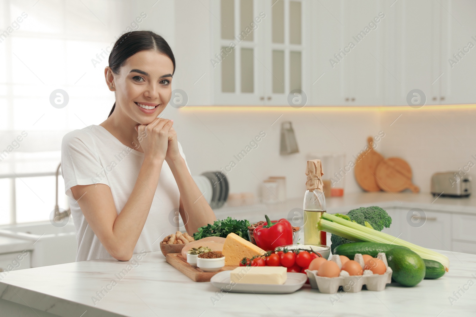 Photo of Happy woman with different products in kitchen. Keto diet