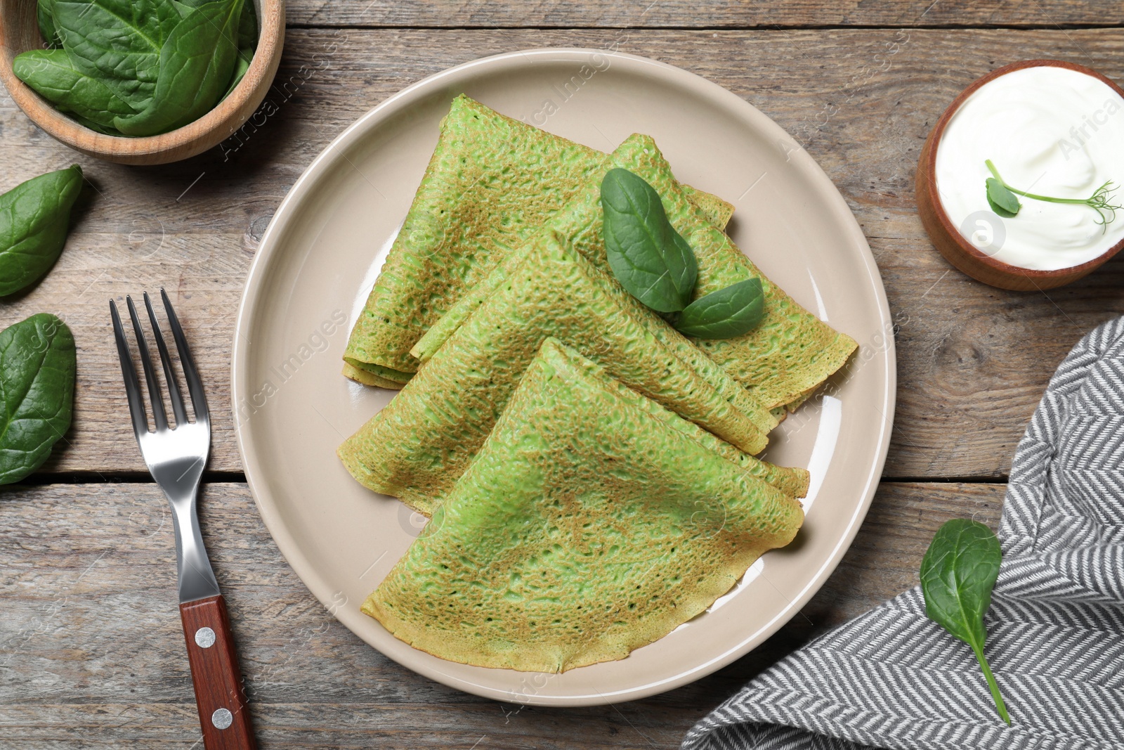 Photo of Delicious spinach crepes served on wooden table, flat lay