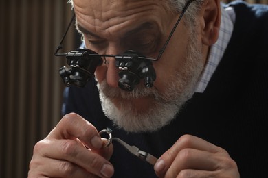 Professional jeweler working with ring on dark background, closeup