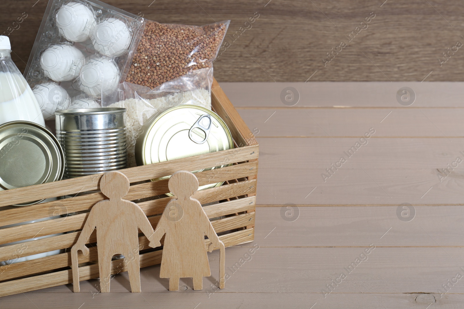 Photo of Humanitarian aid for elderly people. Donation box with food products and figure of senior couple isolated on wooden table, space for text