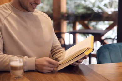 Man with coffee reading book at wooden table, closeup