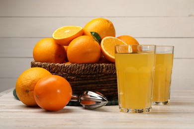 Photo of Many ripe juicy oranges, squeezer and fresh juice on white wooden table