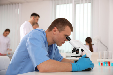 Photo of Scientist using microscope at table and colleagues in laboratory. Medical research
