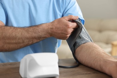 Photo of Man measuring blood pressure at table indoors, closeup