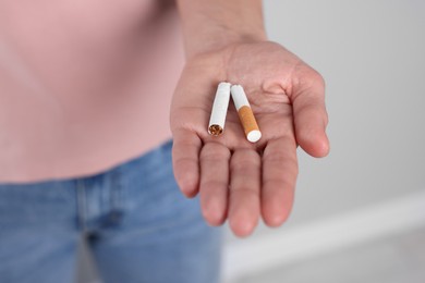 Woman holding broken cigarette on light background, closeup. Quitting smoking concept
