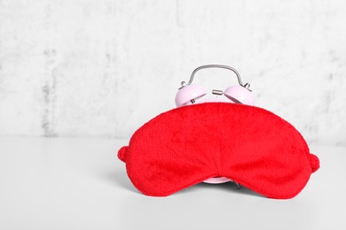 Photo of Red sleep mask and alarm clock on white table. Space for text
