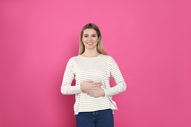 Happy woman touching her belly on pink background. Concept of healthy stomach
