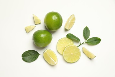 Photo of Whole and cut fresh ripe limes with green leaves on white background, flat lay