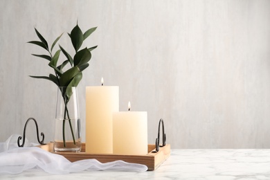 Photo of Beautiful burning candles and vase with green branches on white marble table. Space for text