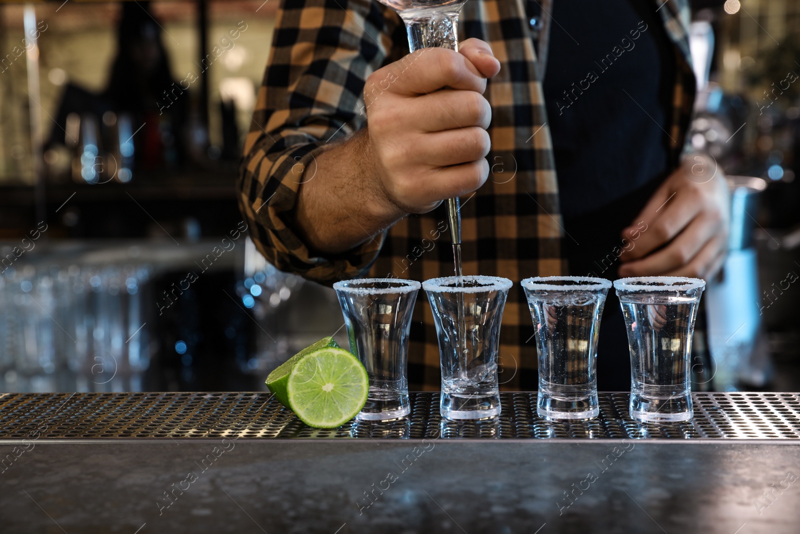 Photo of Bartender pouring Mexican Tequila into shot glasses at bar counter, closeup