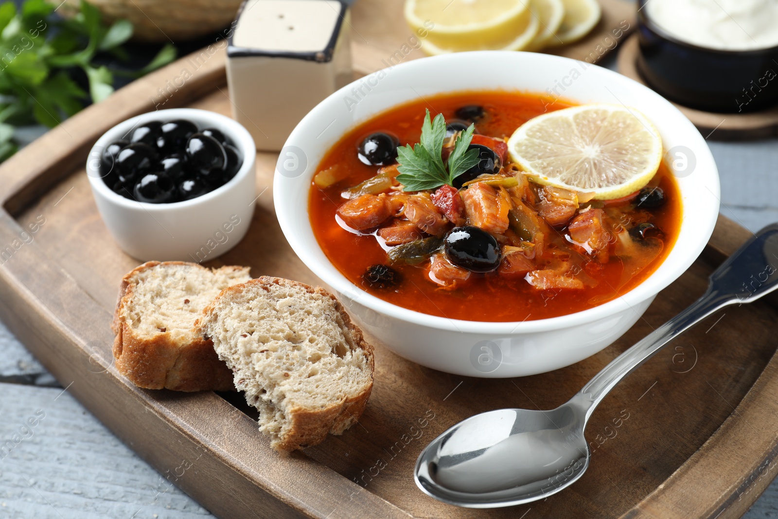 Photo of Meat solyanka soup with sausages, olives and vegetables in bowl served on grey wooden table, closeup