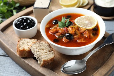 Photo of Meat solyanka soup with sausages, olives and vegetables in bowl served on grey wooden table, closeup