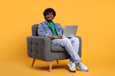 Photo of Smiling man with laptop sitting in armchair on yellow background