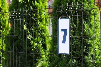 Photo of Plate with house number 7 hanging on iron fence outdoors