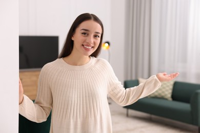 Photo of Happy woman welcoming near white wall at home. Invitation to come in room