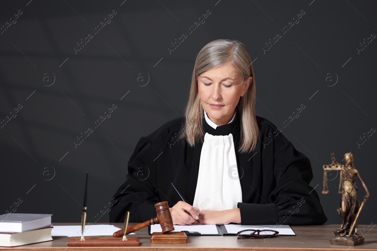 Photo of Judge in court dress working with document indoors. Space for text
