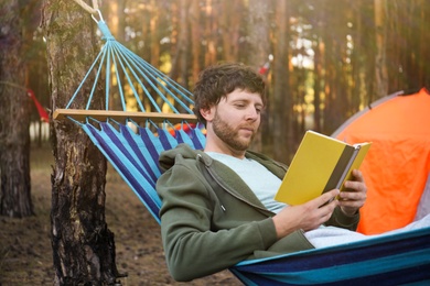 Man with book resting in comfortable hammock outdoors