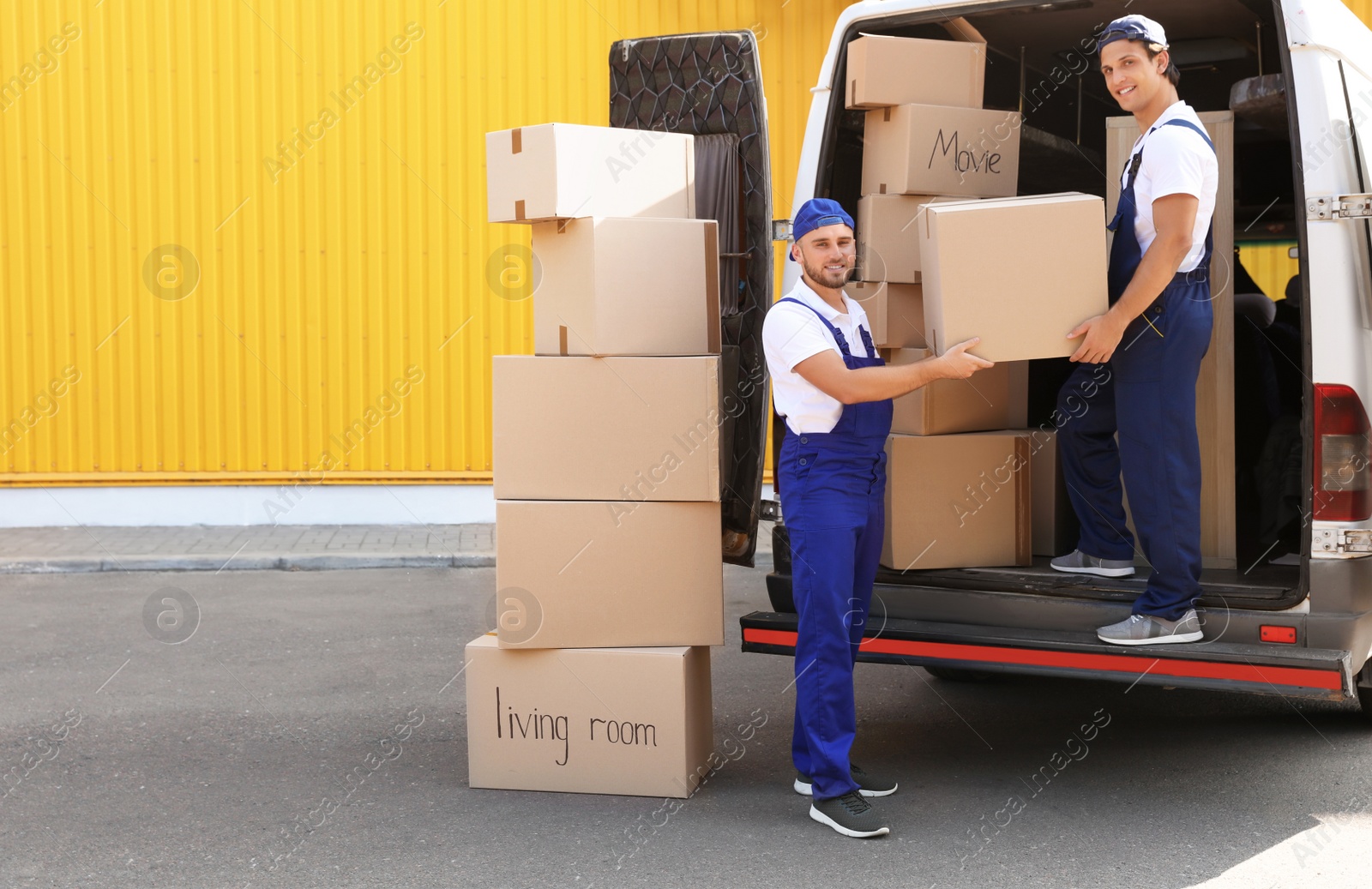 Photo of Male movers unloading boxes from van outdoors