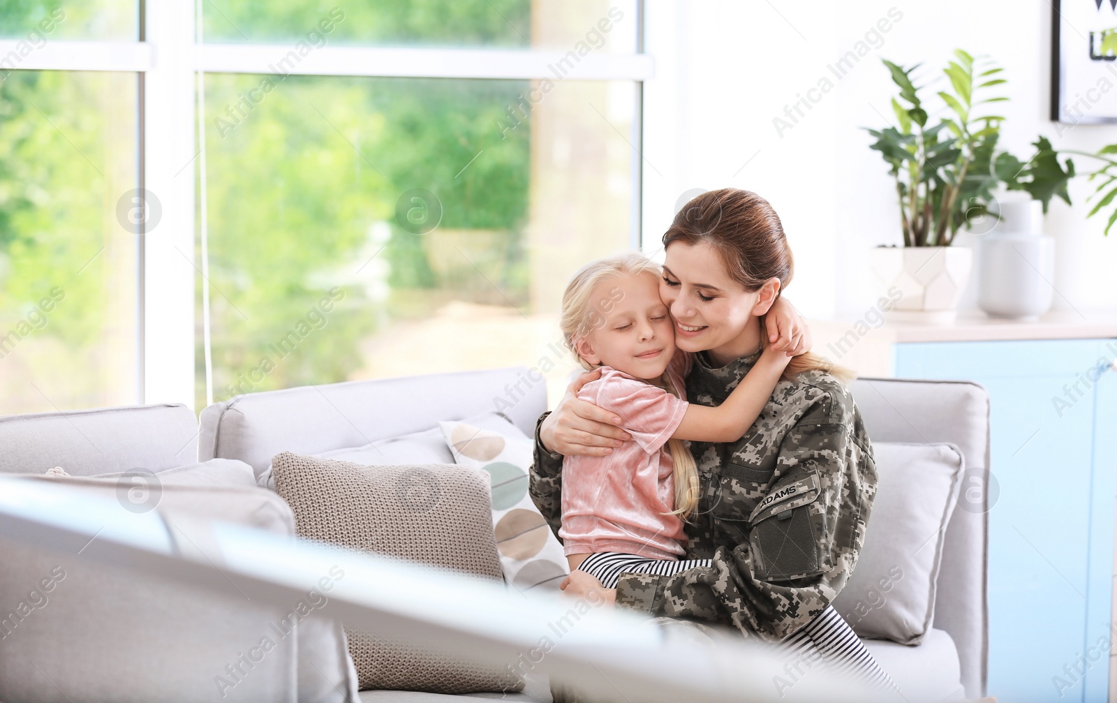 Photo of Woman in military uniform with her little daughter  on sofa at home