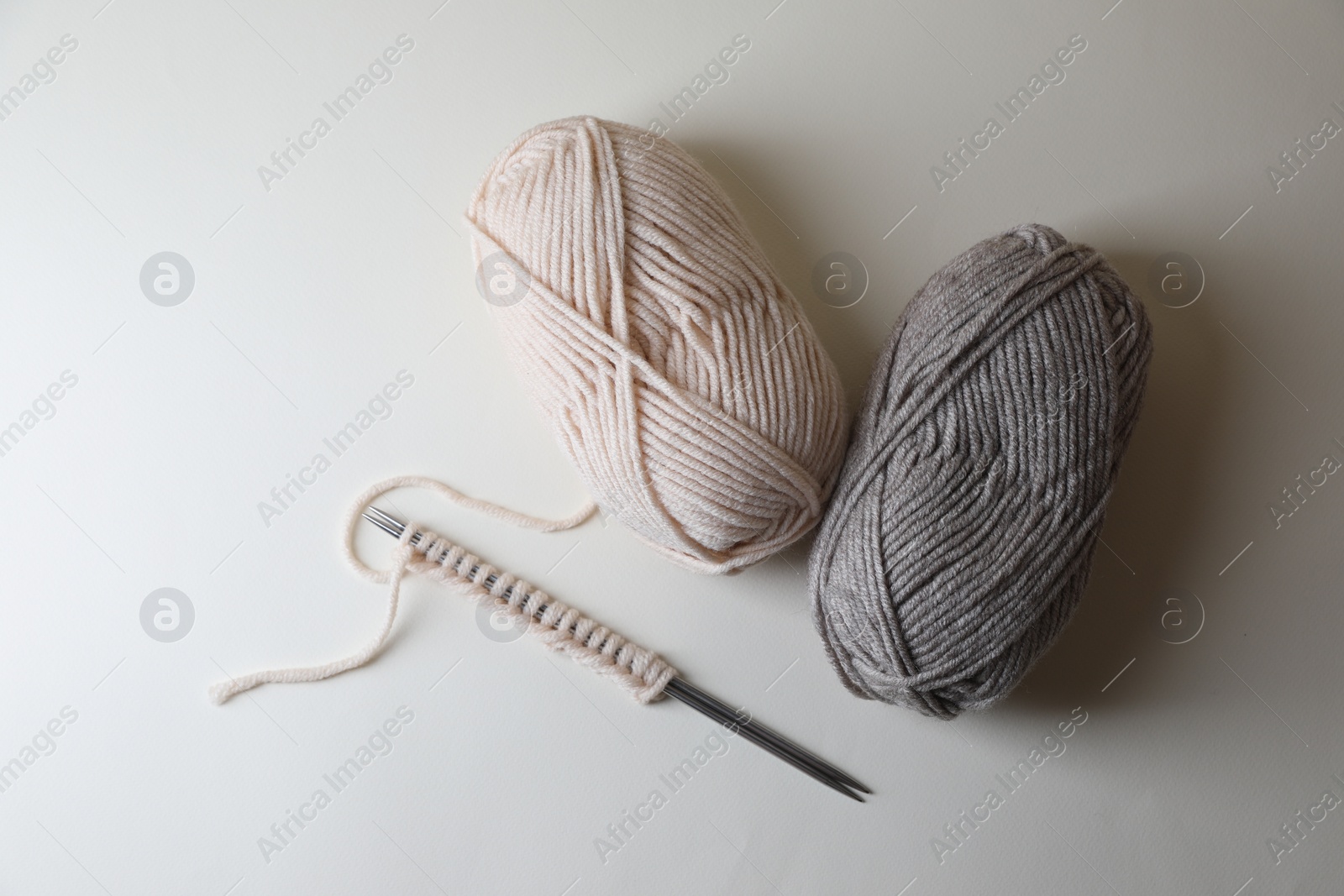 Photo of Soft colorful yarns, knitting and metal needles on light background, flat lay