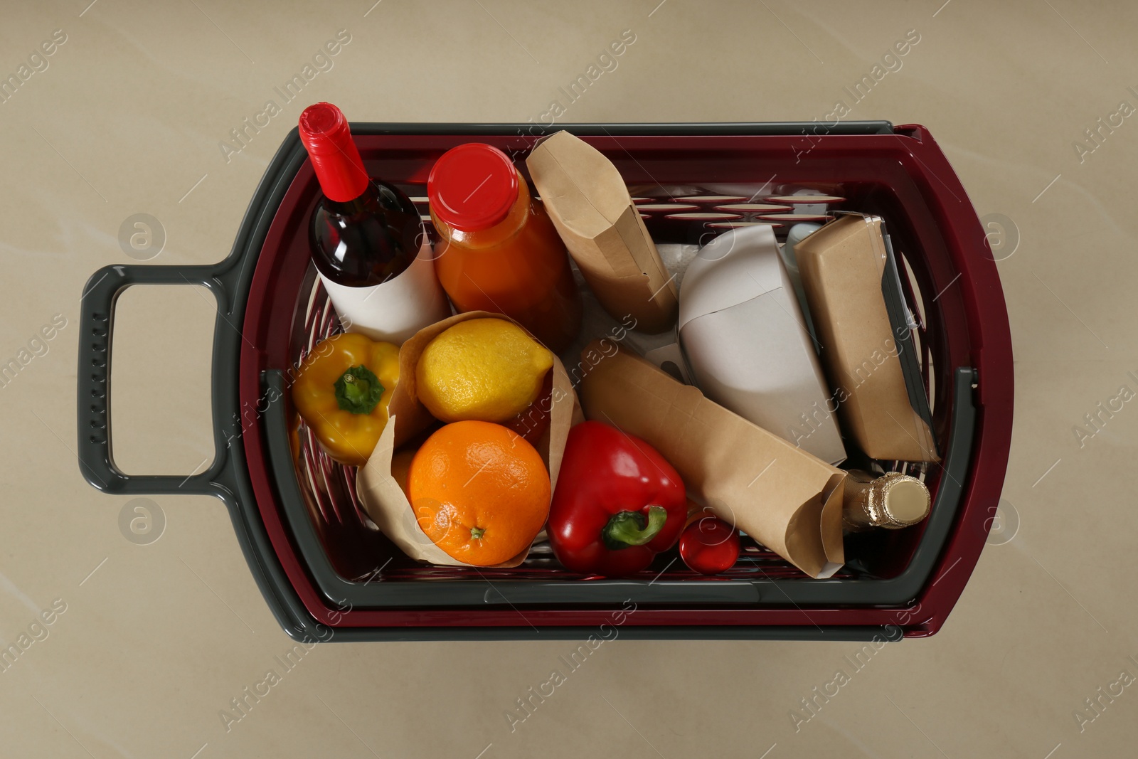 Photo of Shopping basket full of different products on beige tile floor, top view