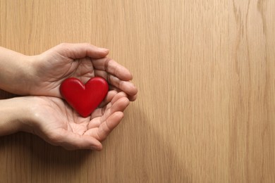 Photo of Elderly woman holding red heart in hands at wooden table, top view. Space for text