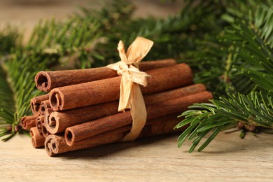 Photo of Bunch of cinnamon sticks and fir branches on wooden table, closeup