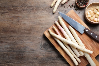 Fresh white asparagus, cutting board and knife on wooden table, flat lay. Space for text