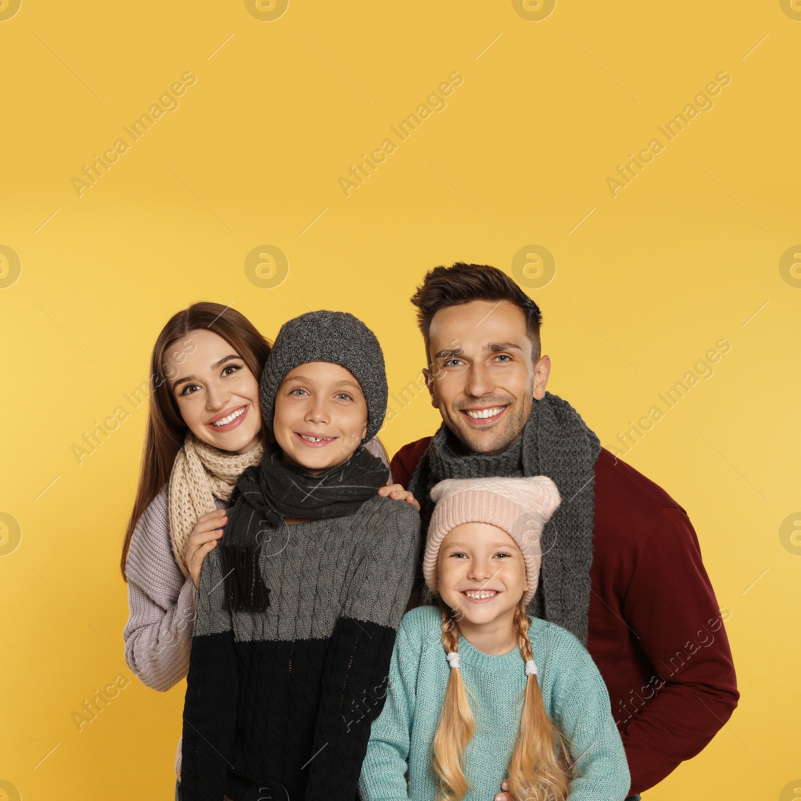 Photo of Happy family in warm clothes on yellow background. Winter season