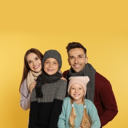 Happy family in warm clothes on yellow background. Winter season