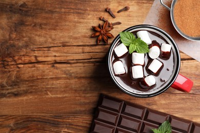 Photo of Mug of delicious hot chocolate with marshmallows and fresh mint near ingredients on wooden table, flat lay. Space for text