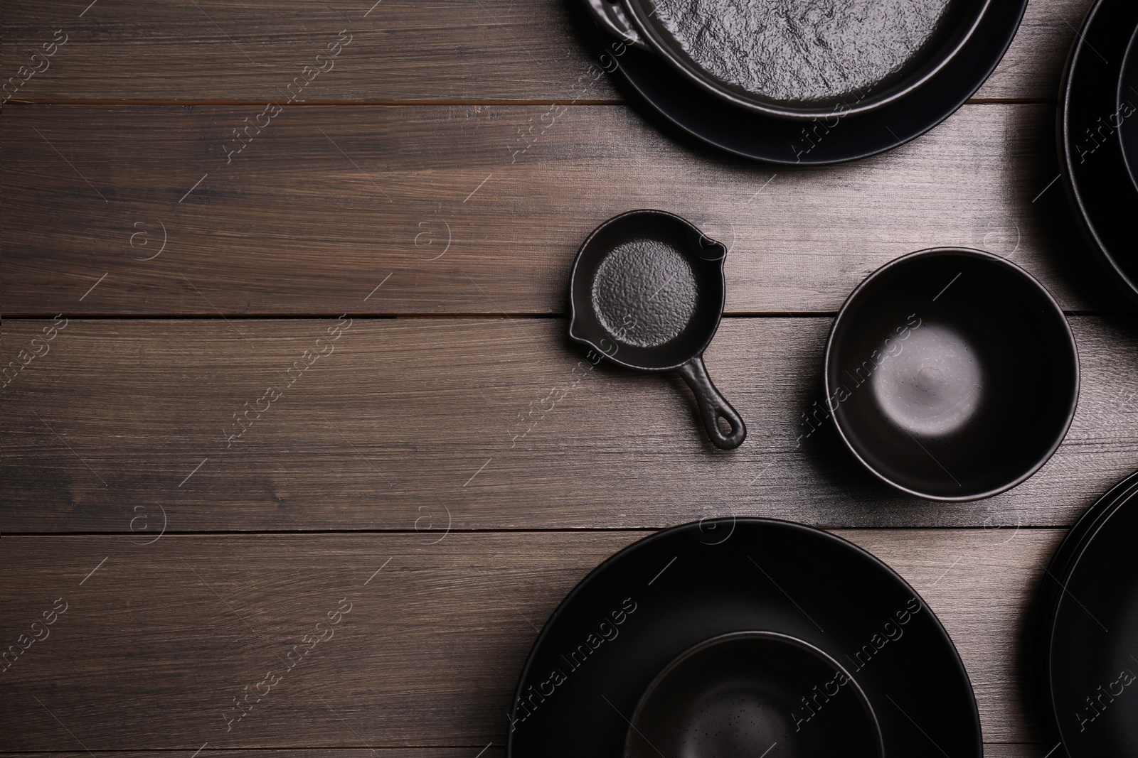 Photo of Different black dishware on wooden table, flat lay. Space for text
