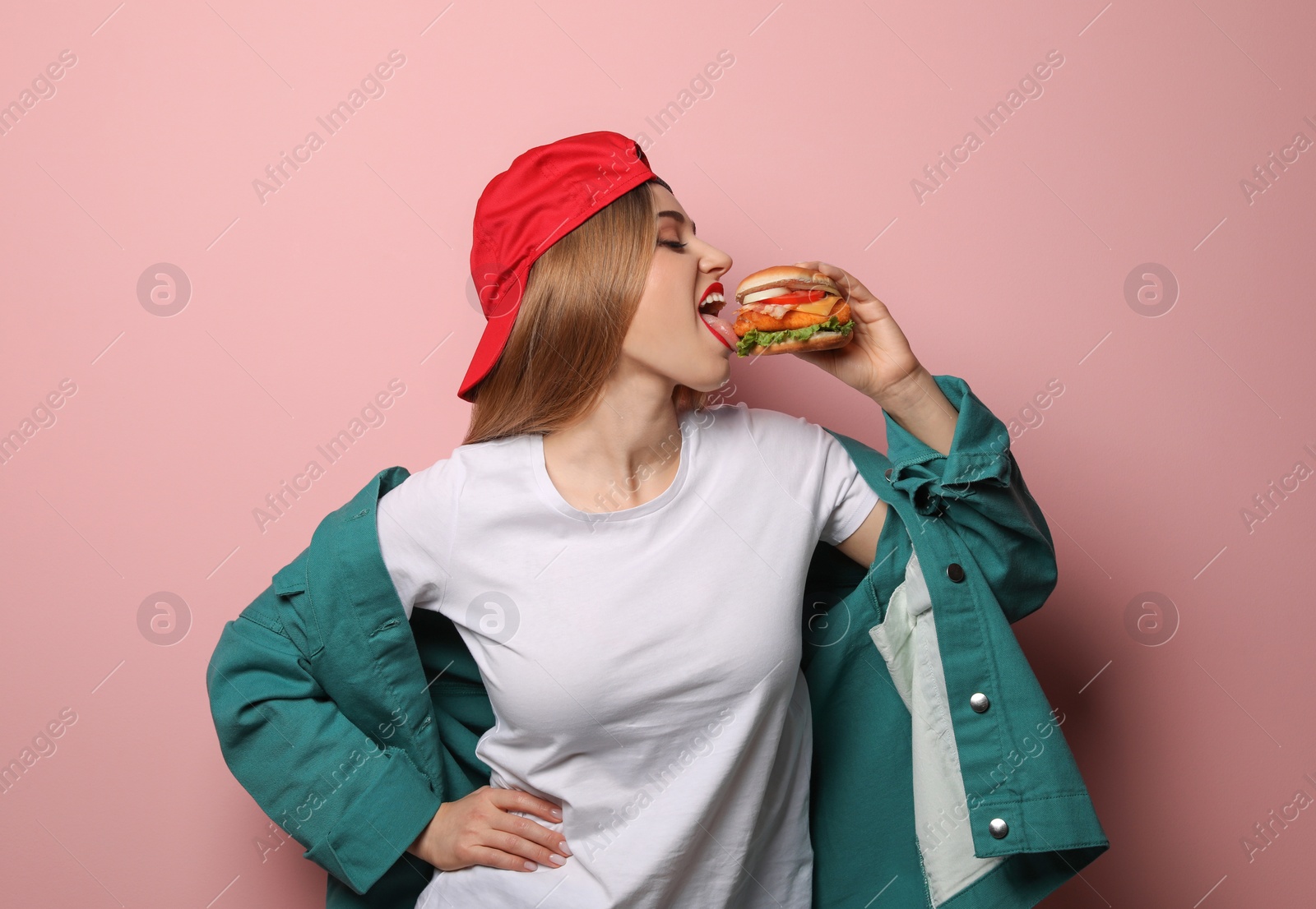 Photo of Pretty woman eating tasty burger on color background