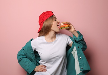 Pretty woman eating tasty burger on color background